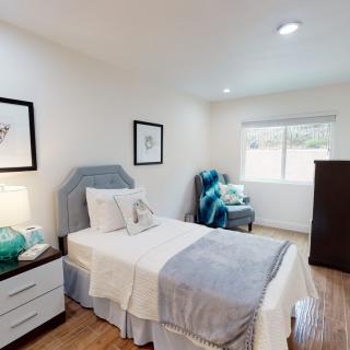 A cozy bedroom with a single bed, nightstand with a lamp, and decorative artwork on the walls.
