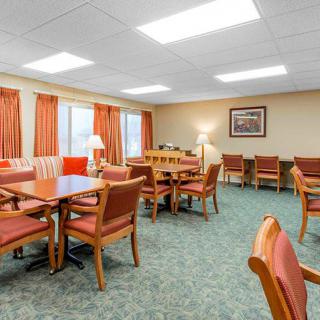 A well-lit dining area with wooden tables and cushioned chairs, featuring a carpeted floor and curtains.