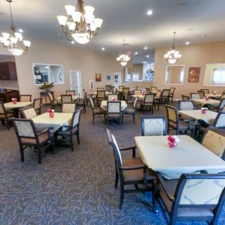A spacious dining room with neatly arranged tables and chairs, illuminated by elegant chandeliers.