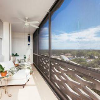 A cozy, screened-in balcony with comfortable seating, plants, and a ceiling fan, overlooking a scenic landscape.