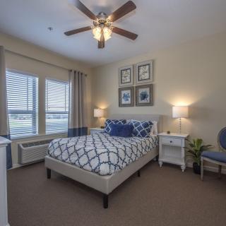 A modern bedroom interior featuring a neatly made bed, stylish decor, and natural light from large windows.