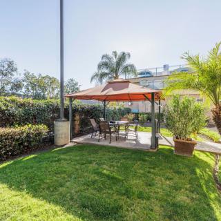A sunny garden with a gazebo and outdoor seating surrounded by lush greenery.
