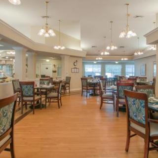 A cozy dining room with neatly arranged tables and chairs, illuminated by elegant chandeliers.