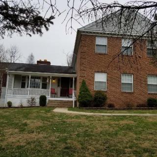 A brick house with a porch and a large lawn in a suburban area.