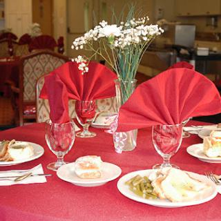 An elegantly set dining table featuring red napkins, decorative flowers, and delicious meals.