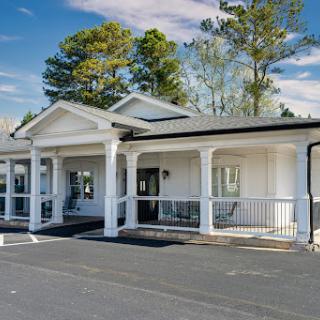 A charming white building with a front porch, surrounded by trees.