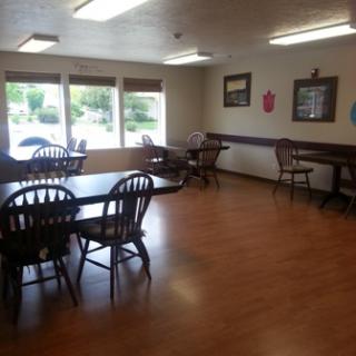 A spacious dining area featuring wooden tables and chairs, illuminated by natural light from large windows.