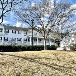 A large white building with black shutters stands behind leafless trees on a sunny winter day.