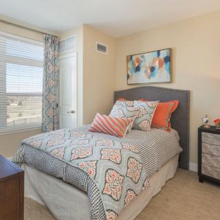 A cozy bedroom with a bed featuring patterned bedding, colorful pillows, a nightstand, and a piece of abstract artwork on the wall.