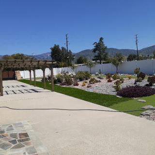A sunny garden with a pergola, patio, and mountainous backdrop.