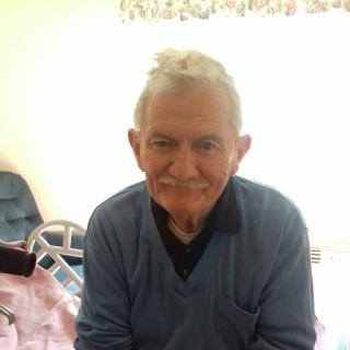 An elderly man with a warm smile, sitting indoors.