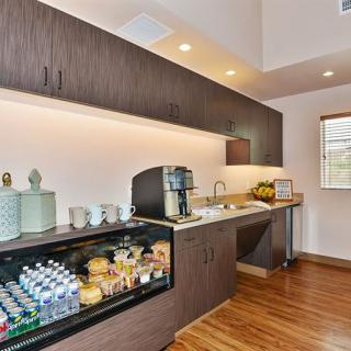 A modern kitchen space featuring a beverage station with a coffee machine, snacks, and a small refrigerator stocked with drinks.