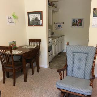 A cozy dining area with a small table, chairs, and an armchair near a compact kitchen.