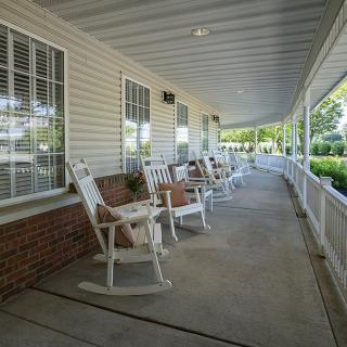 A serene porch with white rocking chairs lined up along a covered patio.