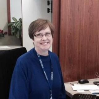 A person smiling while sitting at a desk in an office environment.
