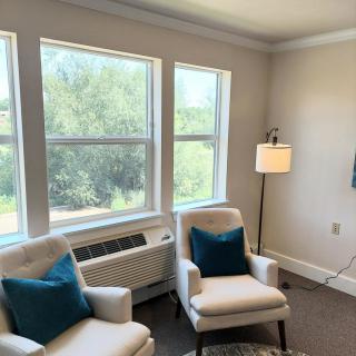 A cozy living room with chairs, a lamp, and large windows providing natural light.