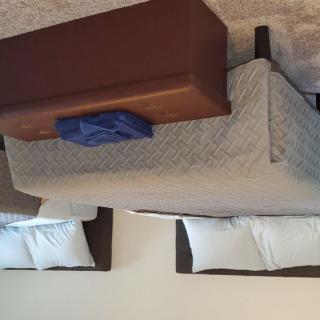 A hotel room with two neatly made beds and a bench at the foot of one bed.