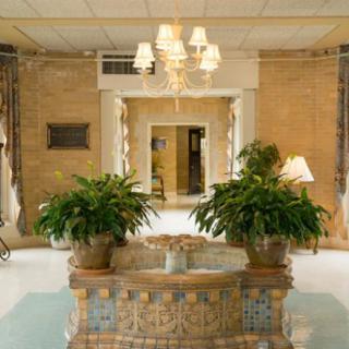 A decorative lobby with a central fountain, plants, and a chandelier.