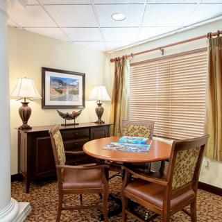A cozy office corner with a round wooden table and two upholstered chairs, accented by elegant lamps and warm-toned decor.