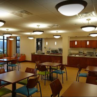 A cozy dining area featuring tables and chairs with a modern design, accompanied by a kitchenette in the background.