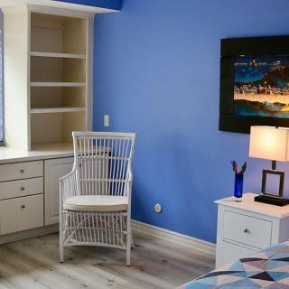 A cozy home office setup with a blue accent wall, featuring a wicker chair, desk with built-in shelving, and a lamp providing warm lighting.