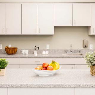 A modern kitchen with white cabinets and a clean countertop featuring a fruit bowl and potted plants.