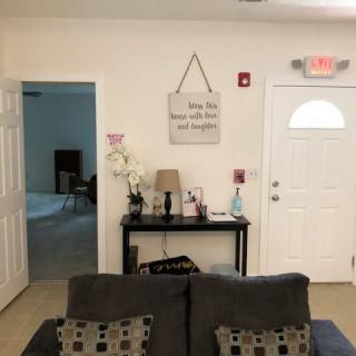 A cozy living room area with a sofa facing a decorated wall featuring a side table, lamp, and wall art.