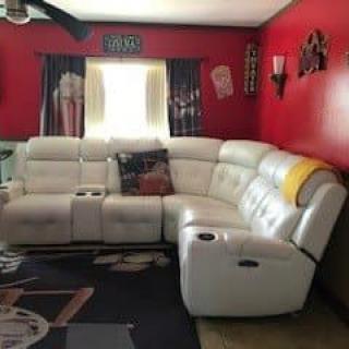 A cozy living room features a white sectional couch against red walls, decorated with wall art and window curtains.