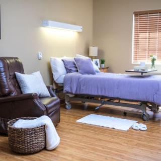 A cozy hospital room designed for comfort, featuring a patient bed with purple bedding and a recliner chair.