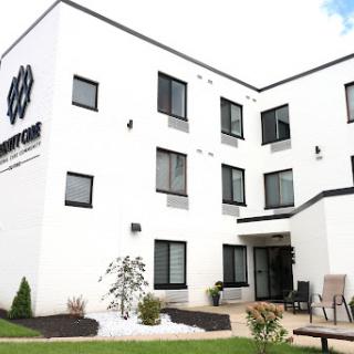 A modern, white building with large windows, featuring a welcoming entrance and landscaped outdoor area.