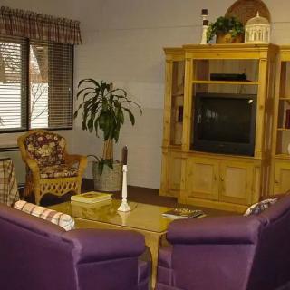 A cozy living room featuring purple chairs, a wooden entertainment unit with a television, and a coffee table, all complemented by a window with natural light.