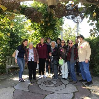 A group of people gathered in a garden under a shaded pergola.