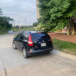 A black Honda parked along a street with lush greenery in the background.