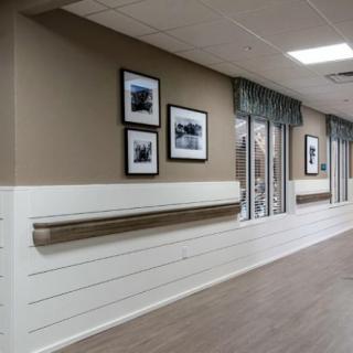A well-lit hallway in a nursing home, featuring framed photographs and handrails along the walls.