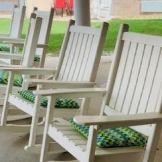 A row of white wooden rocking chairs with green and blue patterned cushions on a porch.