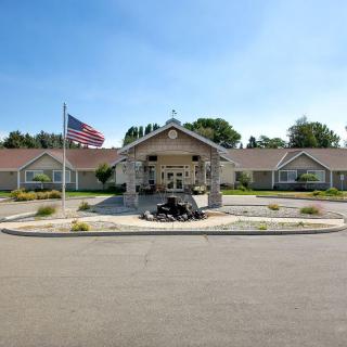 A building entrance with a flagpole in front, surrounded by landscaping on a sunny day.