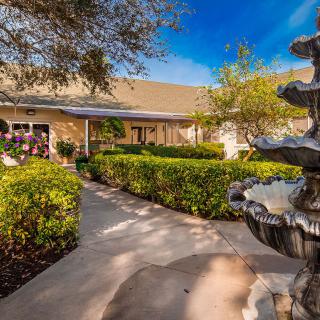 A beautifully landscaped garden with a fountain and pathway leading to a building on a sunny day.