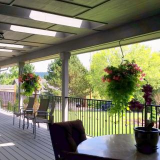 A sunny patio with hanging plants and outdoor furniture overlooking a lush garden.