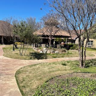 A serene garden setting featuring a winding pathway, trees, and a cozy gazebo under a clear blue sky.