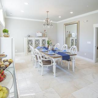 A bright and elegant dining room featuring a long table set with blue accents, a chandelier, and a large wall mirror.