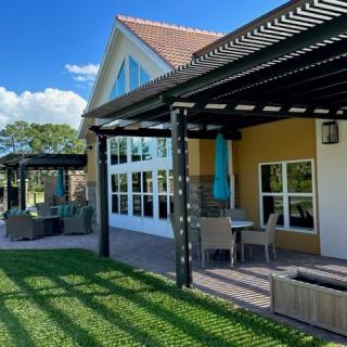 A house with a patio featuring a pergola and outdoor seating, surrounded by a green lawn under a clear blue sky.