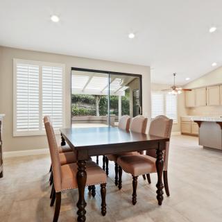 A spacious dining area with a large table and upholstered chairs, overlooking an open kitchen and outdoor patio.