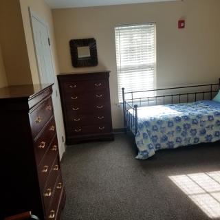 A bedroom with a single bed, two chests of drawers, and a window letting in sunlight.