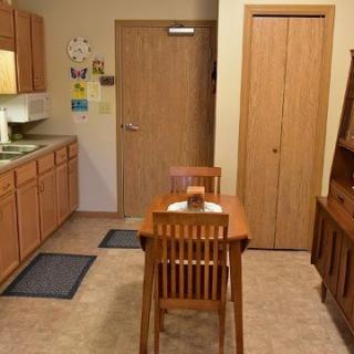 A cozy kitchen with wooden cabinets, a small dining table, and chairs on a linoleum floor.