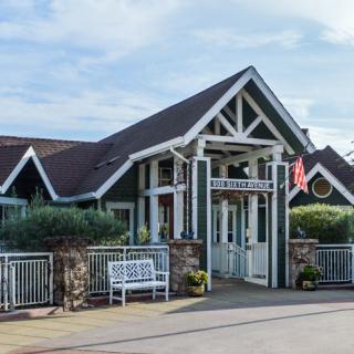 A quaint building with a pitched roof and a welcoming entrance, featuring a bench and potted plants in front.