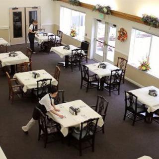 An empty restaurant dining area with neatly set tables and waitstaff preparing the space.