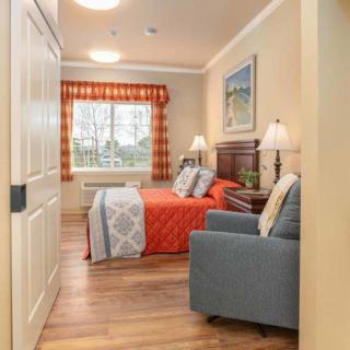 A cozy bedroom with a neatly made bed, bedside lamps, and a large window letting in natural light.
