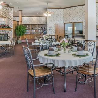 A cozy dining area with elegantly set tables, featuring a warm fireplace and lush greenery.