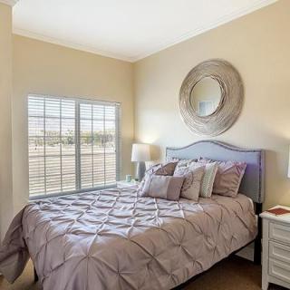 A cozy bedroom with a neatly made bed, featuring a decorative mirror and a lamp near the window.