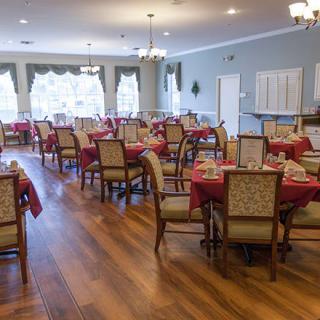 An elegantly decorated dining room with neatly arranged tables and chairs, illuminated by natural light through large windows.
